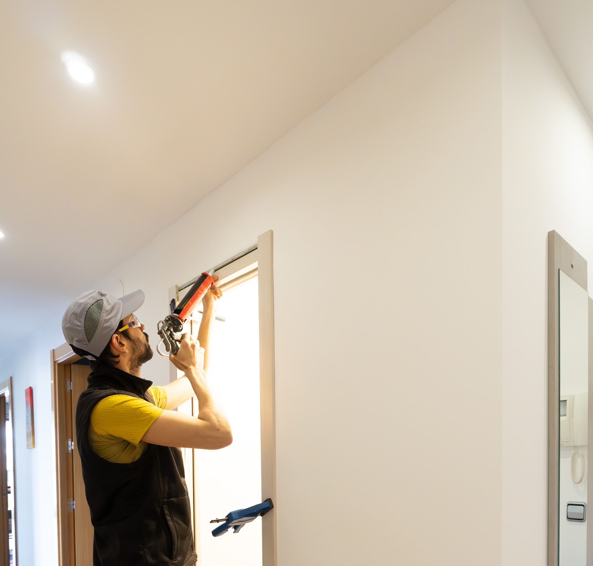 uniformed handyman with work clothes and goggles mounts in a wall hole a door slats. applying silicone and with clamps.